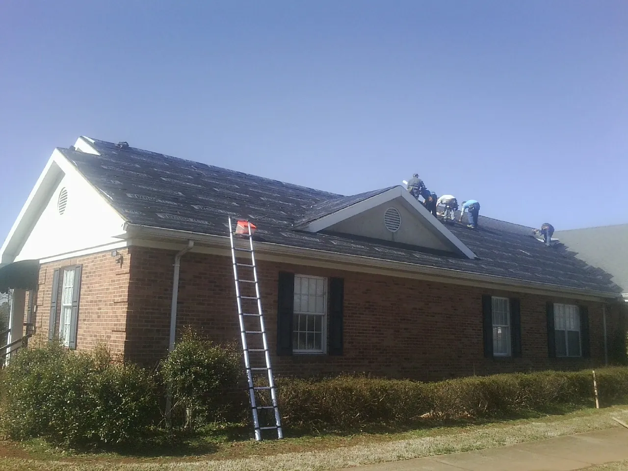 Crew tearing shingles off a brick ranch roof with a ladder set — Metal Roof Repair work by our crew in Pottersville
