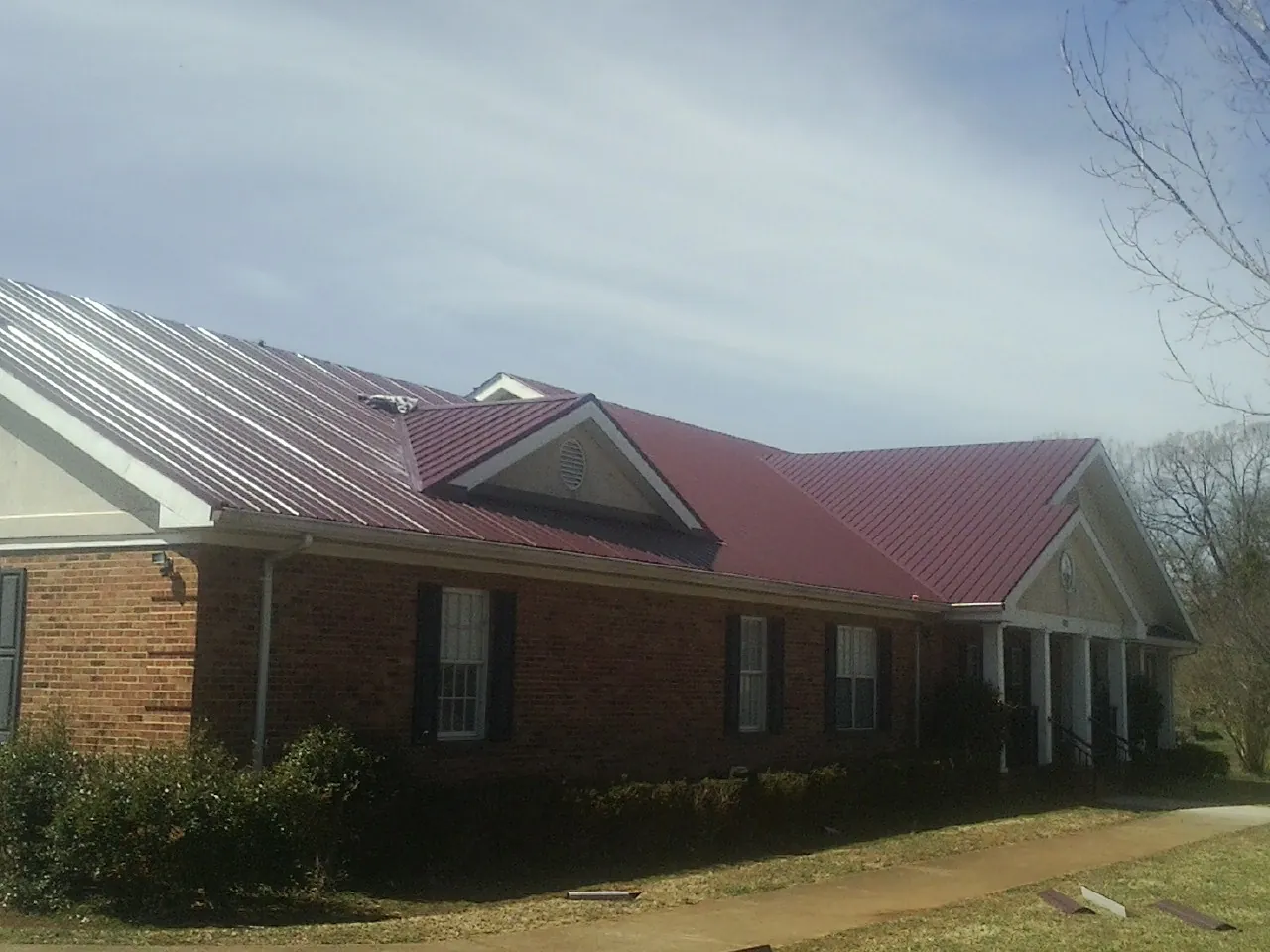 Red metal roof with gabled entries on a long brick building, from a Hail Damage Roof Repair job in Pottersville