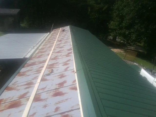 Old rusted panels beside newly installed green metal roofing — Wind Damage Roof Repair by Roofing Brothers in Pottersville