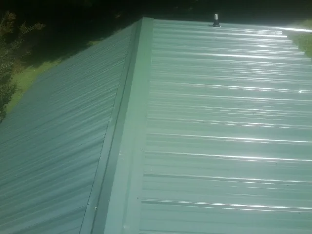 New green metal panels meeting at the ridge of a roof — Flat Roof Repair work by our crew in Pottersville