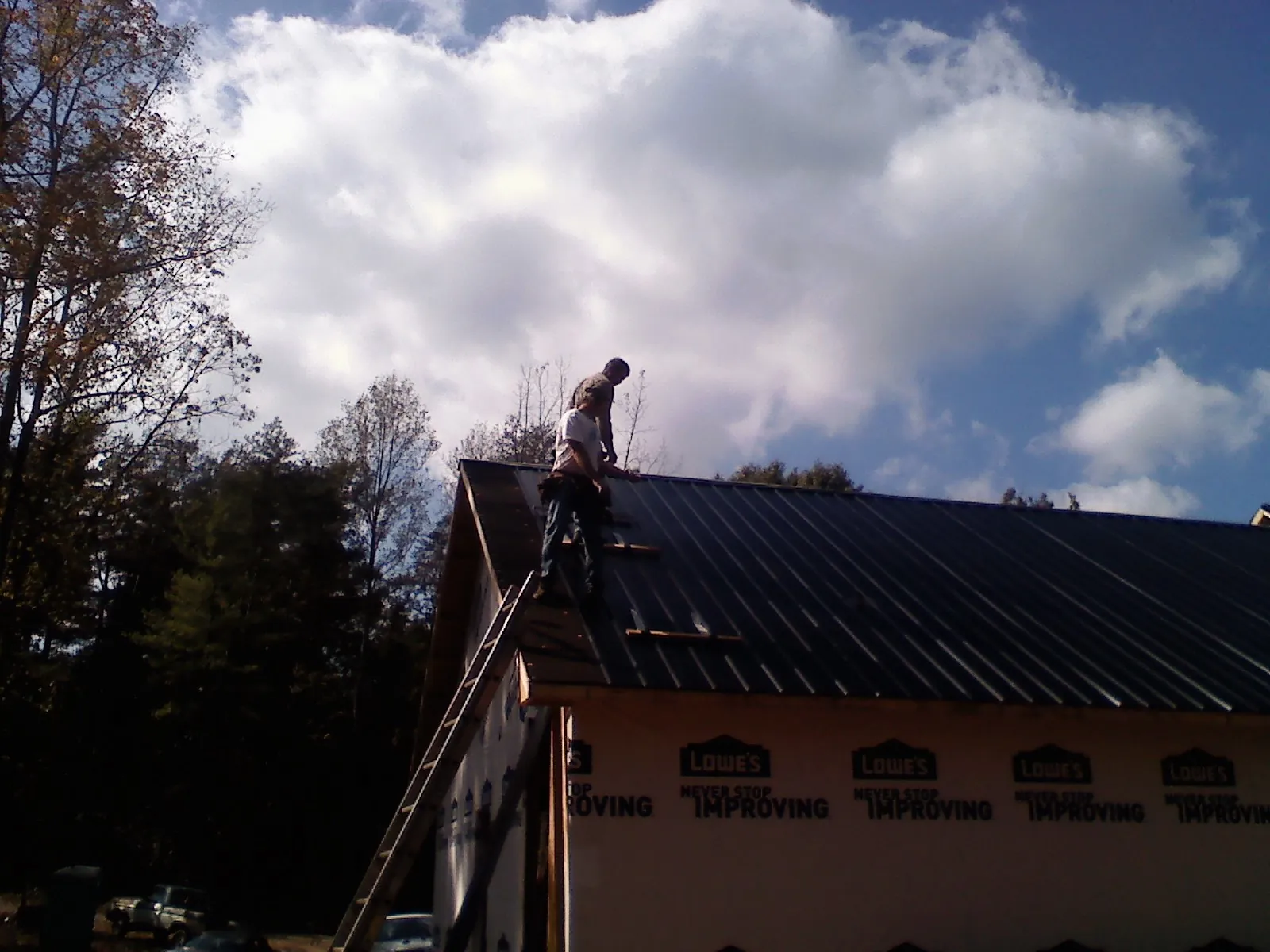 Roofer fastening dark metal panels high against a cloudy sky, from a Roof Inspection job in Pottersville