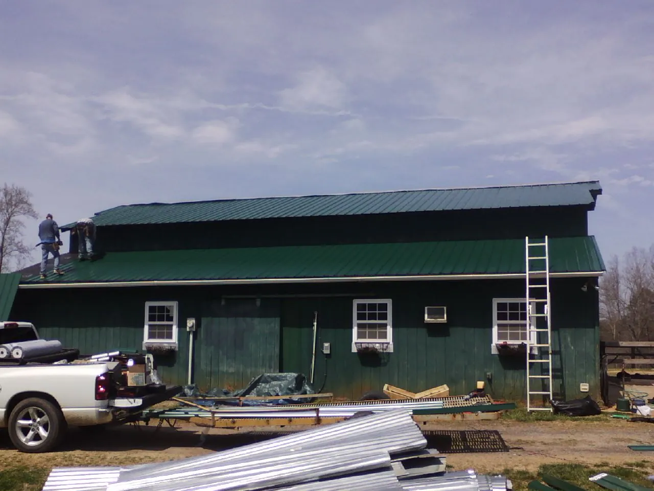 Crew installing green metal roofing on a large green barn in Pottersville