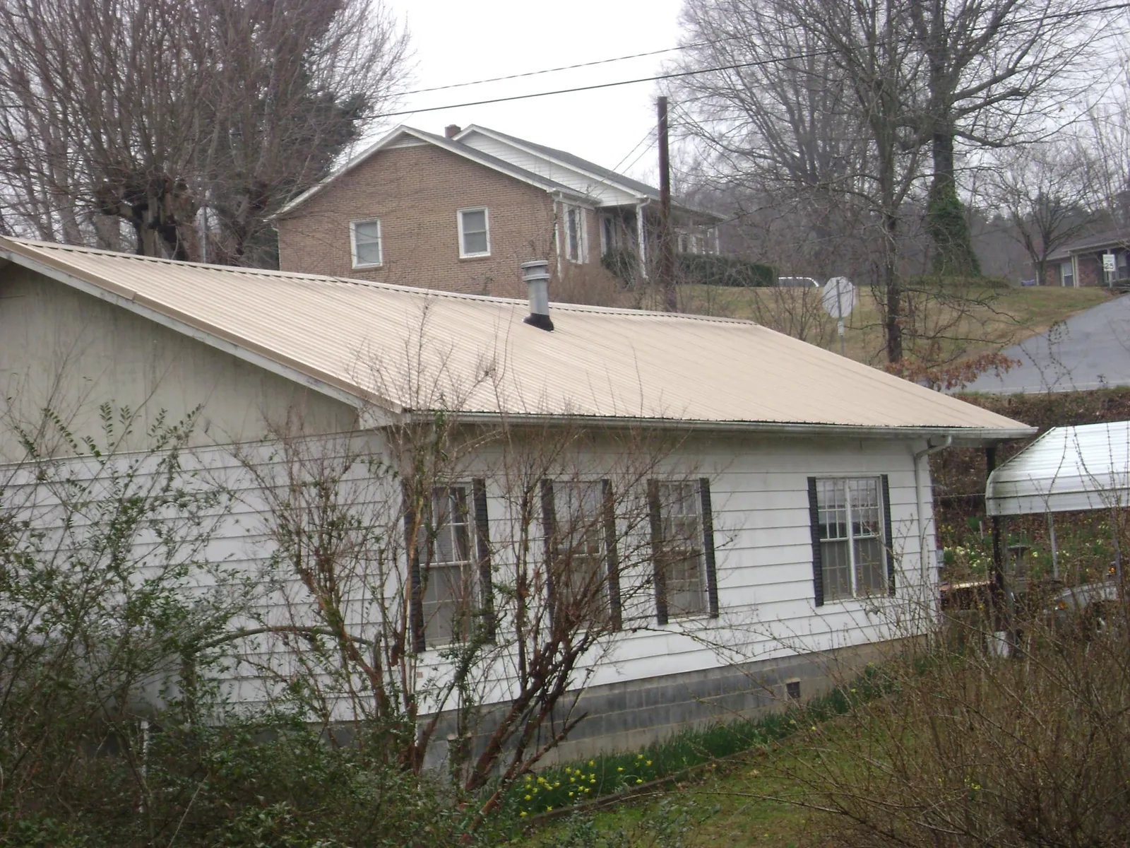 Tan metal roof on a white sided house set into a hillside — Commercial Roofing by Roofing Brothers in Pottersville